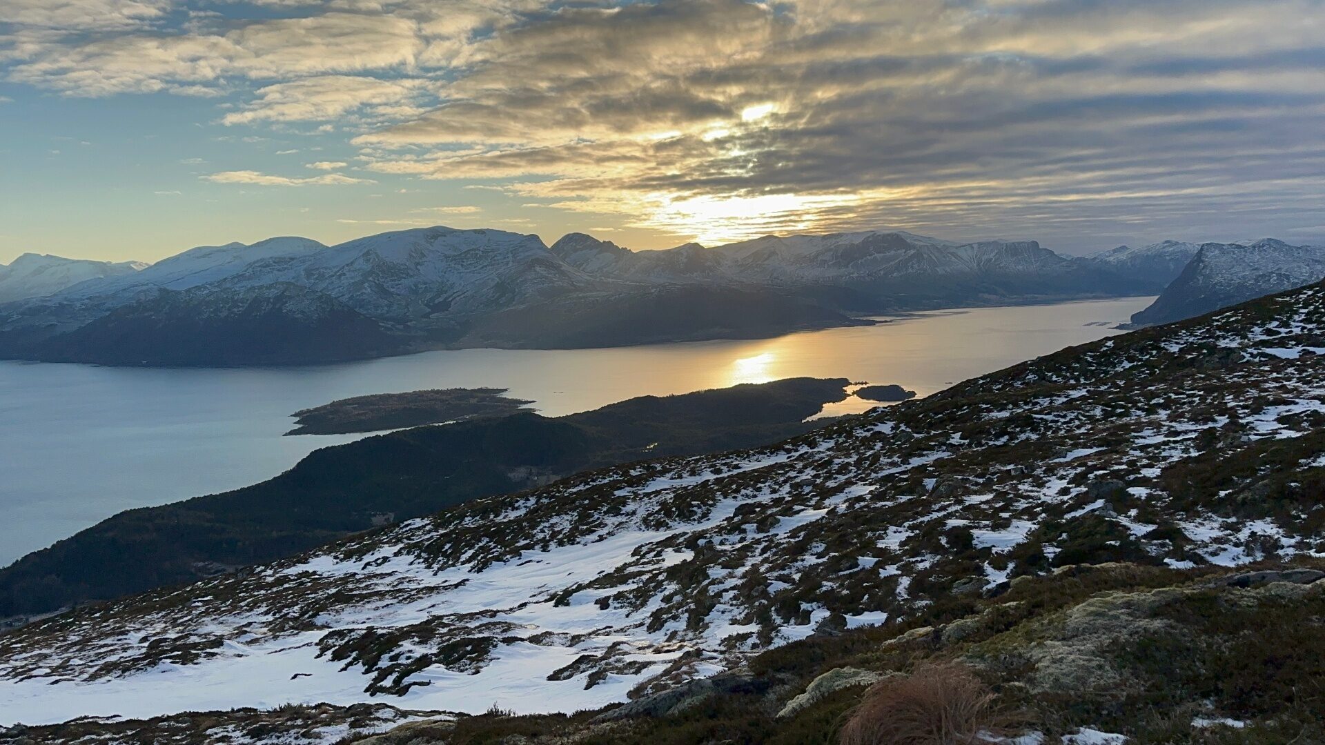 Vinterlys over Vartdalsfjorden med snødekte fjell og sol som speglar seg i sjøen