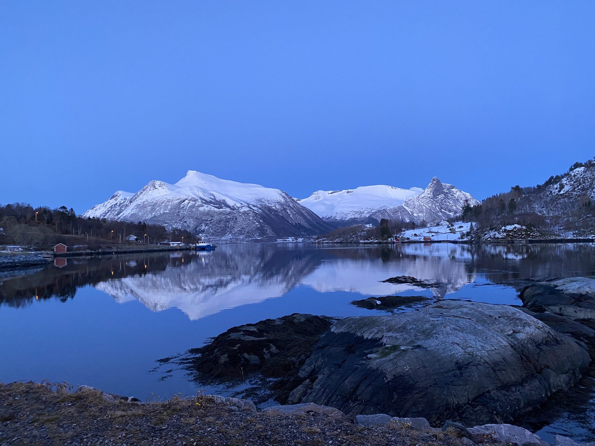 Snødekte fjell speglar seg i blank fjord i blåtimen