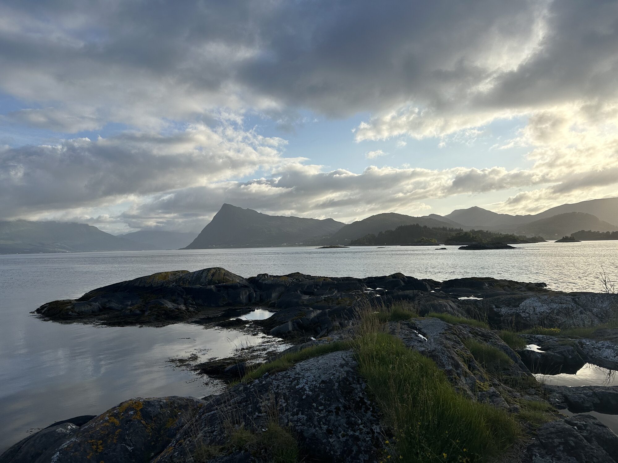 Svaberg og fjord med fjell i bakgrunnen på ein overskya sommarkveld